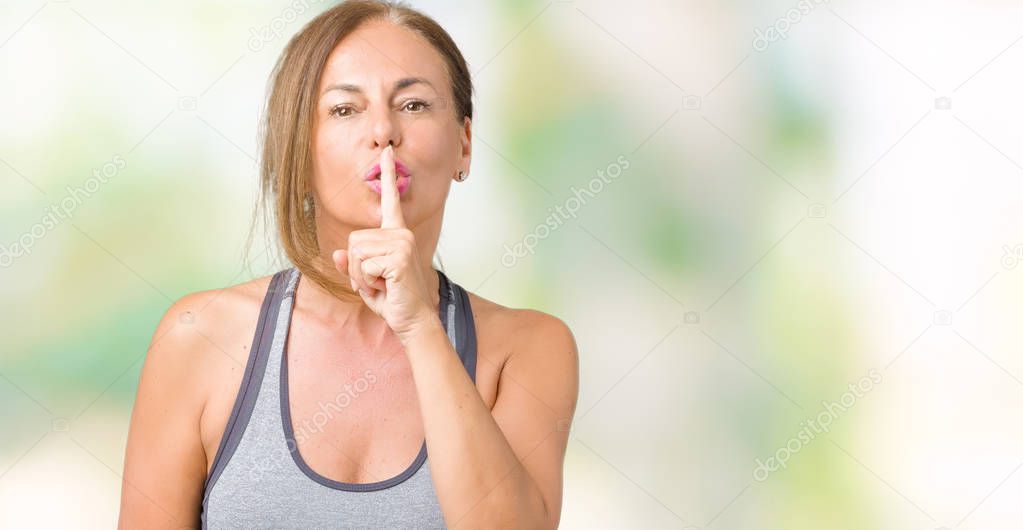 Beautiful middle age woman wearing sport clothes over isolated background asking to be quiet with finger on lips. Silence and secret concept.