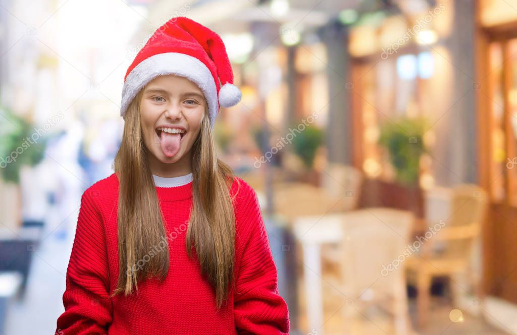 Young beautiful girl wearing christmas hat over isolated background sticking tongue out happy with funny expression. Emotion concept.
