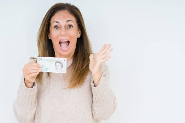 5 pound banknot büyük gülümseme ile çığlık zaferini kutluyor ve ellerini kaldırdı izole arka plan çok mutlu ve heyecanlı, kazanan ifade üzerinde tutan orta yaş kadın
