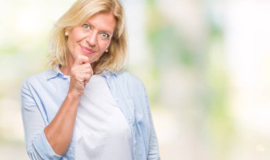 Orta yaş sarışın kadın izole arka plan emin çapraz kollar ve çeneme kaldırdı el ile gülümseme ile kameraya bakıyor. Pozitif düşünce.