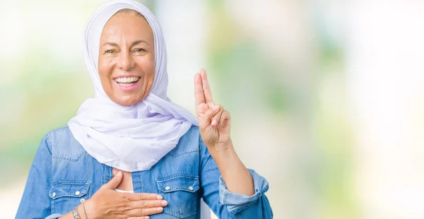 Middle age eastern arab woman wearing arabian hijab over isolated background Swearing with hand on chest and fingers, making a loyalty promise oath