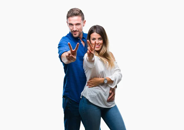 年轻夫妇在爱的孤立背景微笑着看着相机显示手指做胜利标志 第二个 — 图库照片