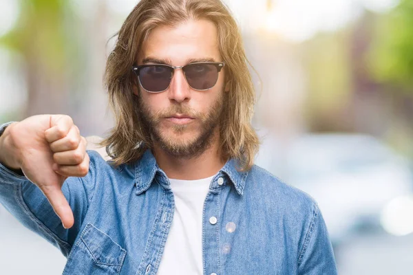 Kızgın yüz, eksi işareti aşağı antipati başparmak ile gösterilen, ret kavramı ile smartphone kullanarak ileti gönderme izole arka plan üzerinde uzun saçlı yakışıklı delikanlı