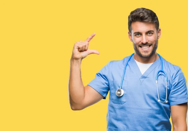 年轻英俊的医生外科医生男子在孤立的背景微笑和自信的手势与手做大小标志与手指 而看和相机 测量概念 — 图库照片