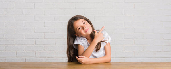 Молодой латиноамериканец сидит дома, веселый, с улыбкой на лице, указывающей рукой и пальцем в сторону, со счастливым и естественным выражением лица, смотрящим в камеру.
.