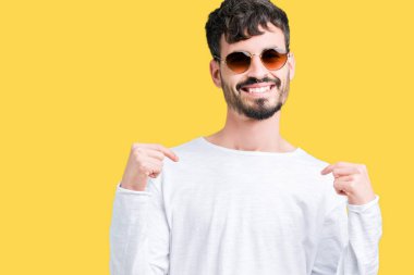 Yakışıklı delikanlı yüzünde gülümseme ile kendinden emin görünüyorsun, kendini gururlu ve mutlu parmakları ile işaret izole arka plan üzerinde güneş gözlüğü takıyor.