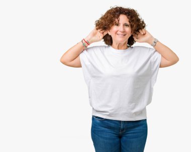 İzole arka plan gülen çekerek kulakları parmaklar, komik jest ile üzerine beyaz t-shirt giyen güzel orta ager kadın kıdemli. Seçmelere sorun