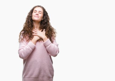 Güzel esmer kıvırcık saçlı Genç kız göğüs kapalı gözlerle ellerinde ve yüzünde minnettar jest ile gülümseyen izole arka plan üzerinde pembe kış kazak giyiyor. Sağlık kavramı.