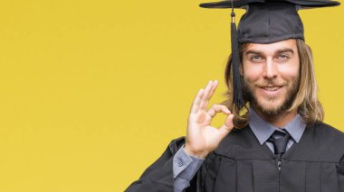 Genç yakışıklı erkek gülümseyen izole arka plan üzerinde uzun saçlı el ve parmaklar ok işaretiyle yapıyor olumlu mezun oldu. Başarılı ifade.