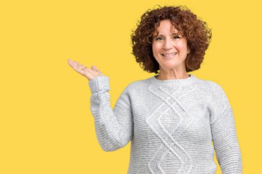 Neşeli sunulması ve kameraya bakarak avucunun ile işaret gülümseyen izole arka plan üzerinde kış kazak giyen güzel orta ager üst düzey kadın.