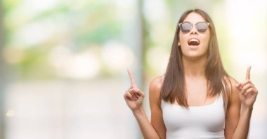 Genç güzel İspanyol güneş gözlüğü takıyor hayrete ve yukarıya bakıyor ve parmakları ile işaret ve silah kaldırdı şaşırttı.