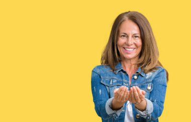 Casual denim ceket izole üzerinde giyen güzel orta yaş kadın alma veya jest vererek birlikte el avuç içi ile gülen arka plan. Ayrı tutma ve koruma