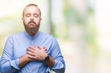 Göğüs kapalı gözler ve yüzünde minnettar jest ile izole arka plan ile gülümseyen üzerinde genç beyaz hipster adam eller. Sağlık kavramı.