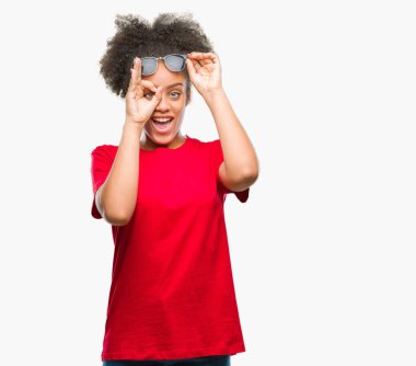 Genç afro Amerikalı kadın gülümsüyor, parmakları ile mutlu yüz üzerinden seyir göz el ile ok jest yapıyor izole arka plan üzerinde güneş gözlüğü takıyor.