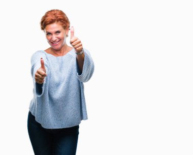 El ile pozitif jest yapıyor onaylama izole arka plan üzerinde kış kazak giyen Atrractive üst düzey beyaz Kızıl saçlı kadın başparmak gülümseyen ve başarı için mutlu. Kamera, kazanan jest arıyorsunuz.