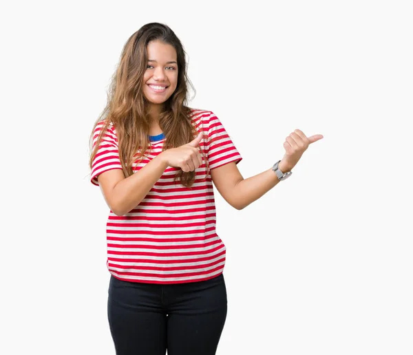 年轻美丽的黑发女人穿着条纹 T恤在孤立的背景指向后面的背后 手和竖起大拇指 面带微笑自信 — 图库照片