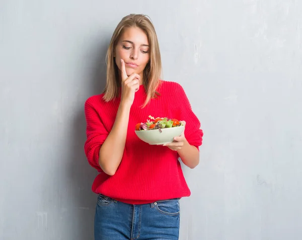 グランジ グレーの美しい若い女性壁に関する質問は 非常に混乱して考え食べるトマト サラダ深刻な顔考えて — ストック写真