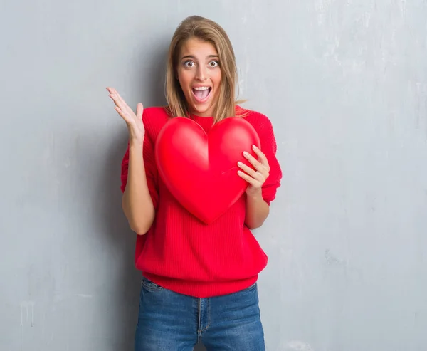 Hermosa Joven Mujer Sobre Pared Gris Grunge Sosteniendo Corazón Rojo — Foto de Stock