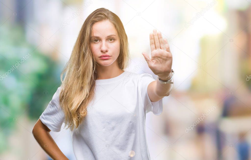 Young beautiful blonde woman wearing casual white t-shirt over isolated background doing stop sing with palm of the hand. Warning expression with negative and serious gesture on the face.