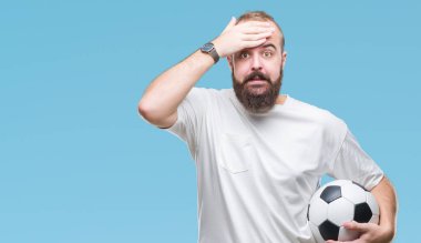 Baş, el ile vurguladı izole arka plan üzerinde futbol futbol topu tutan genç beyaz hipster adam şok utanç ve sürpriz suratla, öfkeli ve sinirli. Korku ve hata için üzgün.