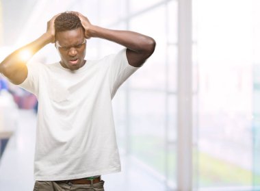 Çünkü çaresiz ve stresli baş ağrısı acı beyaz t-shirt giyen genç Afro-Amerikan adam ağrı ve migren. Ellerini kafasına.