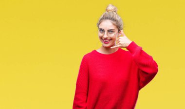 Kırmızı kazak ve gözlük yapıyor gülümseyen izole arka plan üzerinde giyen genç güzel sarışın kadın telefon hareketi ile el ve parmak telefonda konuşuyor gibi. Kavramları iletişim.