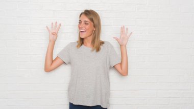 Güzel ve genç birbayan gösterilen ve parmakları ile işaret beyaz tuğla duvarın üzerinden numara 9 kendinden emin ve mutlu gülümseyerek süre.