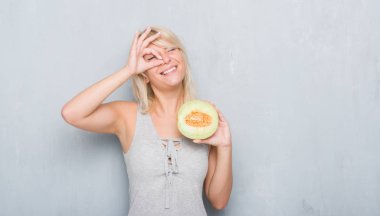 Ok işareti ile el parmaklarının arasından seyir göze yapıyor gülümseyen mutlu yüz ile kavun karpuz yeme grunge gri duvar yetişkin beyaz kadın