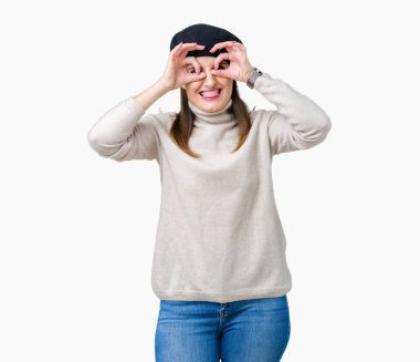 Orta yaş Olgun kadın giyiyor kış kazak ve bere ok jest yapıyor izole arka plan üzerinde dilini, parmaklarının arasından baktığını yapışmasını dürbün gibi. Deli ifade.