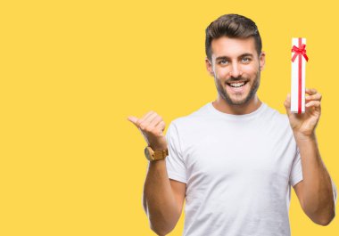 İşaret ve başparmak kadar mutlu yüz gülümseyen tarafı ile gösteren izole arka plan üzerinde Sevgililer günü hediyesi veren aşık genç yakışıklı adam