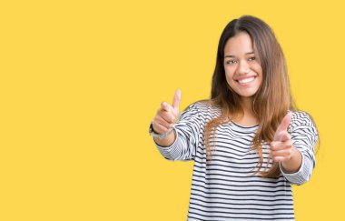 Fotoğraf makinesi ile mutlu ve komik yüz için parmakları işaret izole arka plan üzerinde çizgili süveter giyen genç güzel esmer kadın. İyi enerji ve vibes.