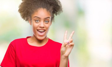 Mutlu yüz zafer işareti yaparken kameraya göz kırpıyor ile gülümseyen izole arka plan üzerinde genç afro Amerikalı kadın. İki numaralı.