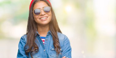 Genç güzel Arap kadın üzerinde güneş gözlüğü takıyor mutlu yüz ile gülümseyerek kameraya seyir silah geçti arka plan izole. Olumlu bir kişi.