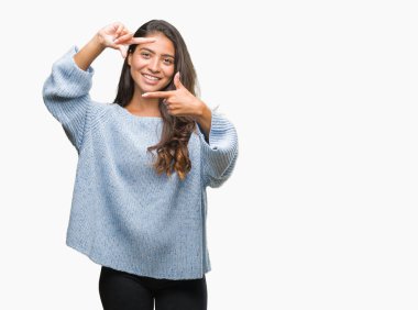 Elle yapma çerçeve ve parmakları ile mutlu yüz gülümseyen izole arka plan üzerinde kış kazak giyen genç güzel Arap kadın. Yaratıcılık ve Fotoğrafçılık kavramı.