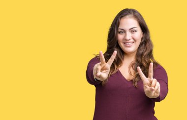 Güzel ve çekici artı boyutu genç kadın parmaklarını zafer işareti yaparken gösterilen kamera seyir gülümseyen izole arka plan üzerinde elbise giyiyor. İki numaralı.