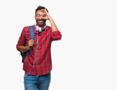 Gülümseyerek el parmakları ile mutlu yüz üzerinden seyir göz ile ok jest yapıyor izole arka plan üzerinde kulaklık ve sırt çantası giyiyor yetişkin İspanyol öğrenci adam.