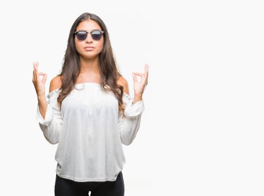 Genç güzel Arap kadın giyiyor güneş gözlüğü izole arka plan üzerinde dinlenmek ve gülümseyen gözlerle kapalı parmak jestle meditasyon yapıyor. Yoga kavramı.