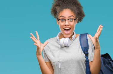 Üzerinde kulaklık ve sırt çantası giyen genç afro Amerikan öğrenci kadın deli kutluyor arka plan izole ve çığlık kaldırdı ve açık gözleri heyecanlı silah ile başarı için hayrete düşürdü. Kazanan kavramı