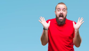 Üzerinde kırmızı gömlek giyen genç beyaz hipster adam deli kutluyor arka plan izole ve başarı için kaldırdı kollarını açarak hayrete ve heyecanlı çığlık gözleri açık. Kazanan kavramı