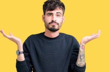 İzole arka plan clueless ve şaşkın bir ifadeyle kollar ve eller kaldırdı genç yakışıklı adam. Şüphe kavramı.