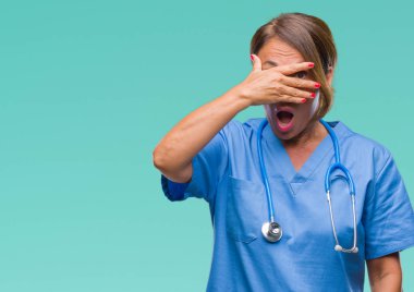 Yüz ve gözler el ile kapsayan şok bakmak izole arka plan orta yaş kıdemli hemşire doktor kadın mahcup ifadeyle parmaklarımın arasından arıyorsunuz.