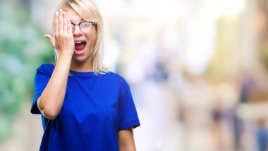 El yüz ve sürpriz duygu kendinden emin gülümseme ile tek gözüyle kapsayan izole arka plan üzerinde gözlük takan genç güzel sarışın kadın.