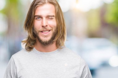 Seksi bir ifadeyle, neşeli ve mutlu yüzünü kameraya bakarak göz kırpıyor izole arka plan üzerinde uzun saçlı yakışıklı delikanlı.