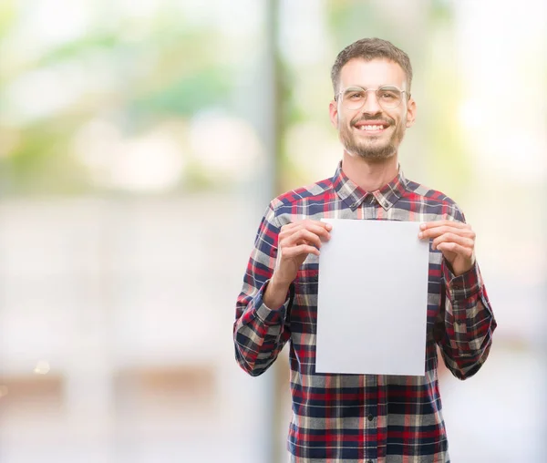 年轻的时髦成人男子拿着空白纸表与一个幸福的脸站在微笑着自信的微笑显示牙齿 — 图库照片