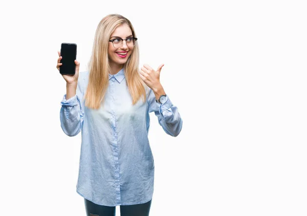 年轻美丽的金发女商人显示屏幕的智能手机在孤立的背景指向和显示与快乐的脸微笑的一侧与拇指 — 图库照片