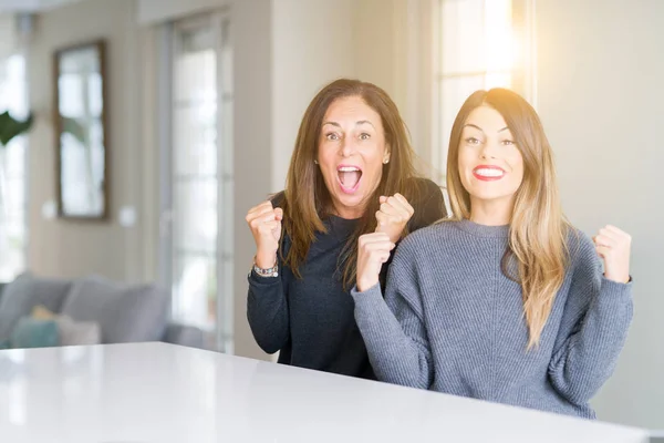 Beautiful family of mother and daughter together at home celebrating surprised and amazed for success with arms raised and open eyes. Winner concept.