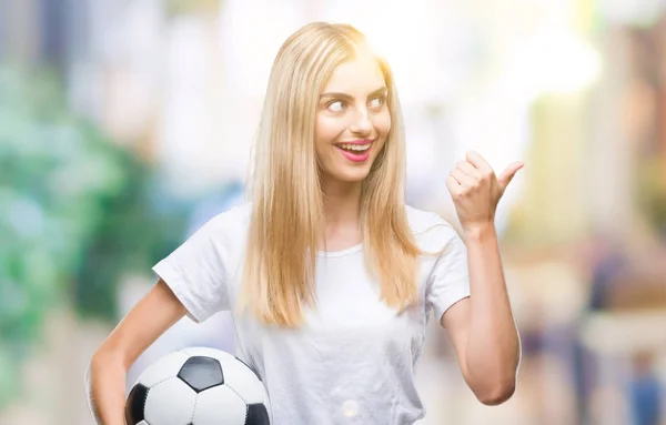 指していると幸せそうな顔を笑顔で側まで親指で示す分離の背景にサッカー ボールを保持している若い美しいブロンドの女性 — ストック写真