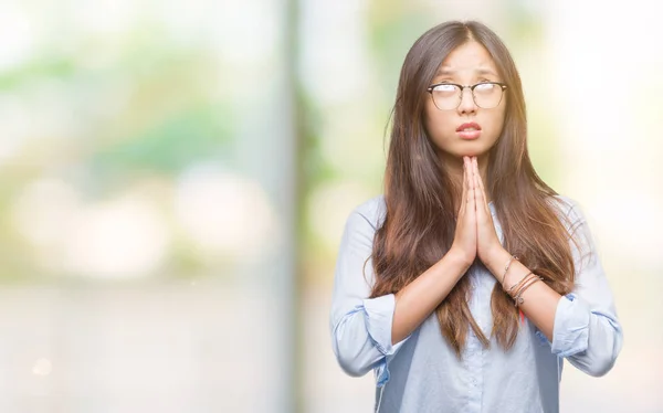 Young asian business woman wearing glasses over isolated background begging and praying with hands together with hope expression on face very emotional and worried. Asking for forgiveness. Religion concept.