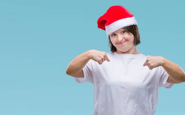 带着唐氏综合症的年轻成年妇女戴着圣诞帽在与世隔绝的背景下 脸上带着微笑 用手指自豪和快乐地指着自己 — 图库照片