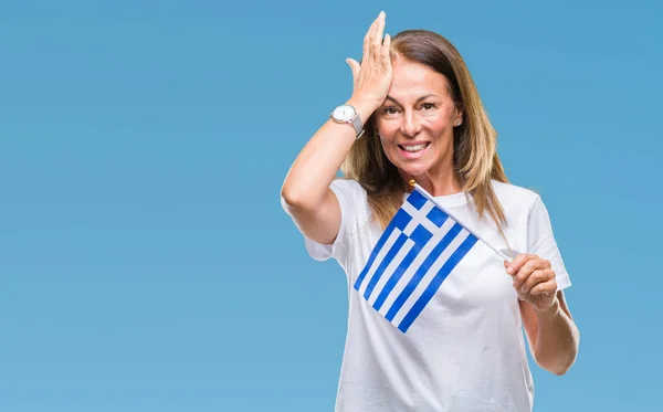 Middle age hispanic woman holding flag of Greece over isolated background stressed with hand on head, shocked with shame and surprise face, angry and frustrated. Fear and upset for mistake.